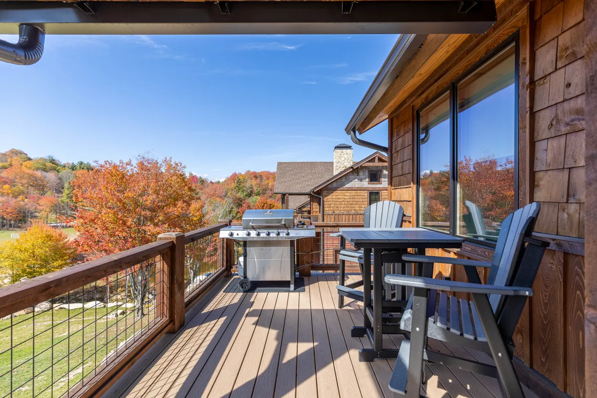 A charming deck scene with outdoor seating, a wooden railing, and an outdoor grill, all framed by rich autumn foliage. The space feels both private and expansive, perfect for enjoying meals, drinks, or quiet contemplation with nature all around.