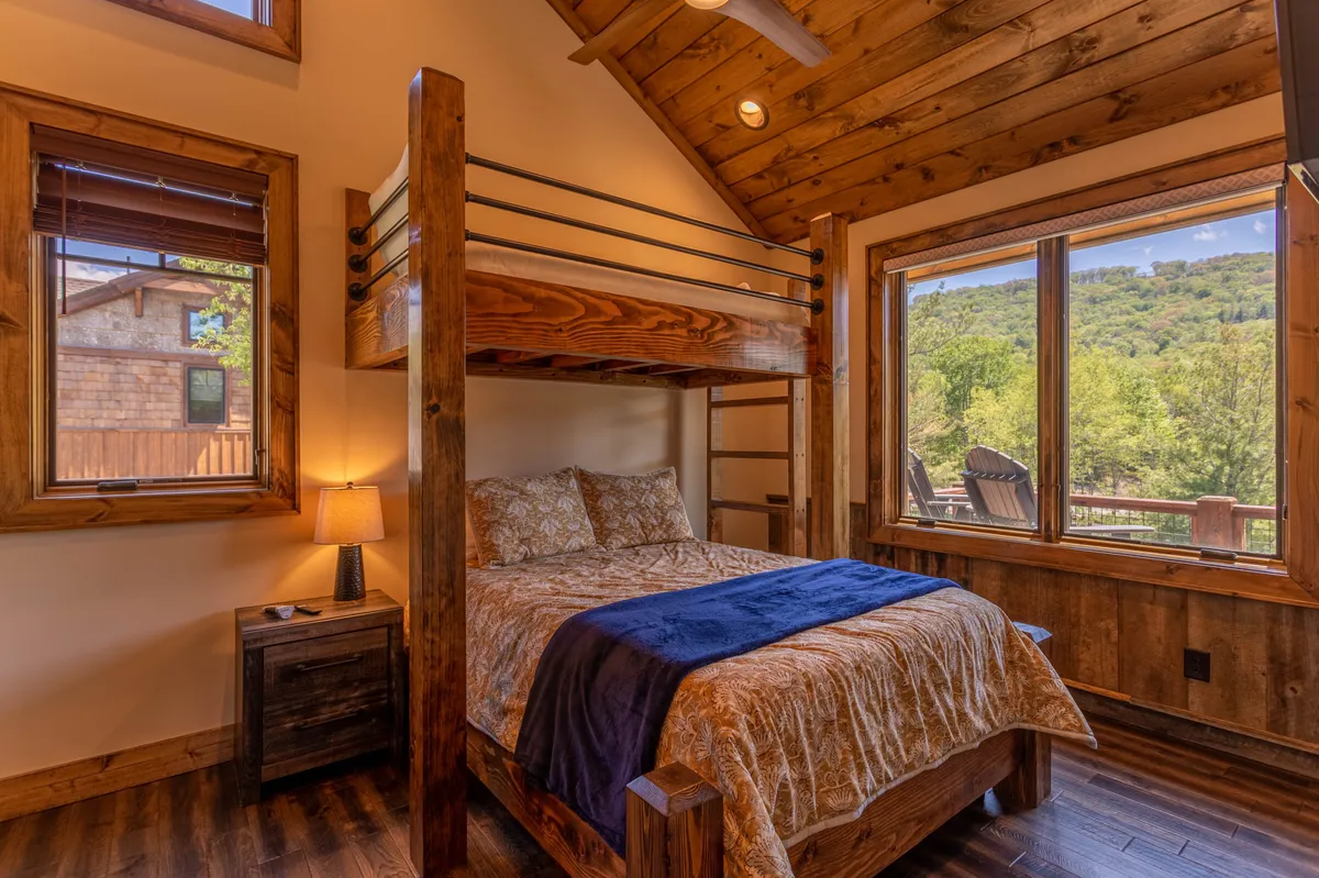 A bright and welcoming bedroom with a bunk bed, large windows that let in natural light, and a nightstand with a lamp. The setup is ideal for families or groups, and the view outside creates a peaceful atmosphere.