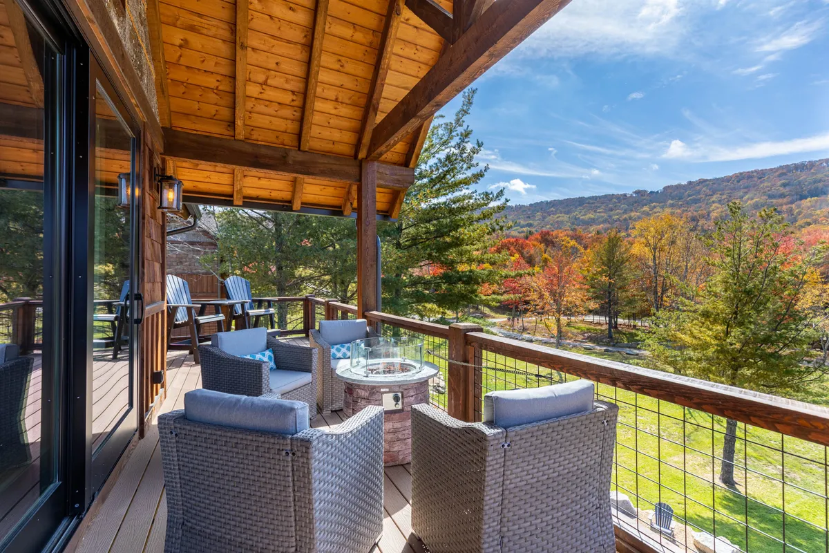 An inviting exterior scene with a cozy outdoor seating area set against colorful autumn trees and a backdrop of distant mountain views. Adirondack chairs are arranged to encourage relaxation and conversation, evoking the experience of unwinding outdoors. The peaceful mood is enhanced by hints of stargazing and evenings by a fire.