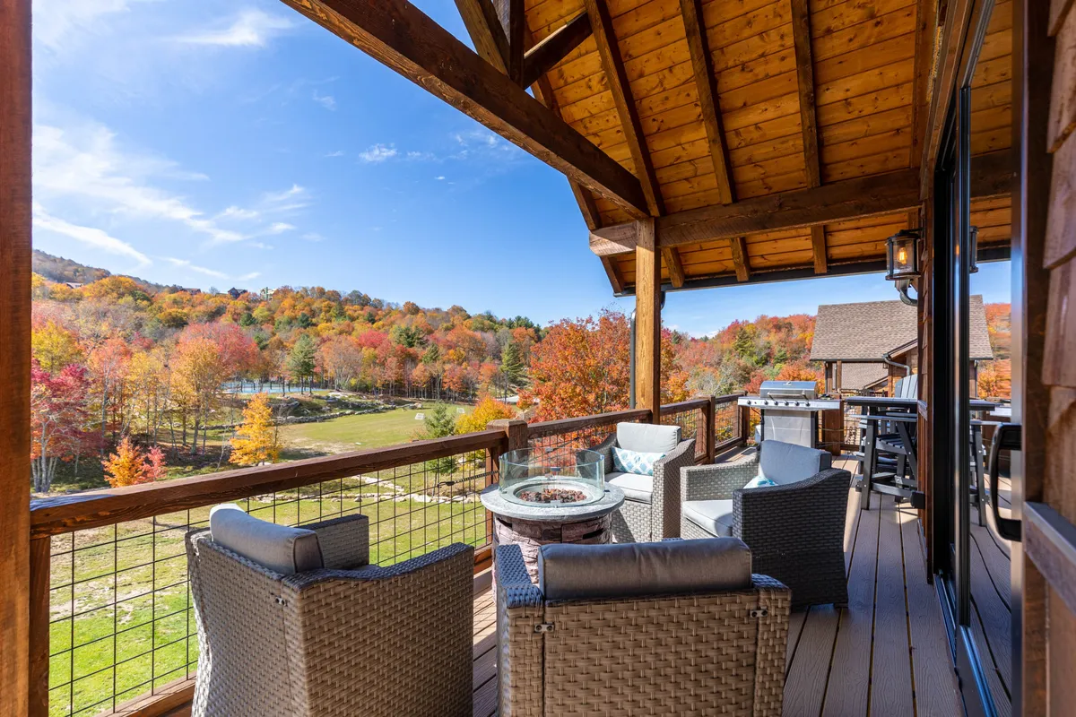 A tranquil exterior setting featuring a circle of chairs around a fire pit, overlooking a panoramic expanse of colorful trees. The scene invites social gatherings, morning coffee, and cozy fireside chats, all with a mountain vista as the backdrop.