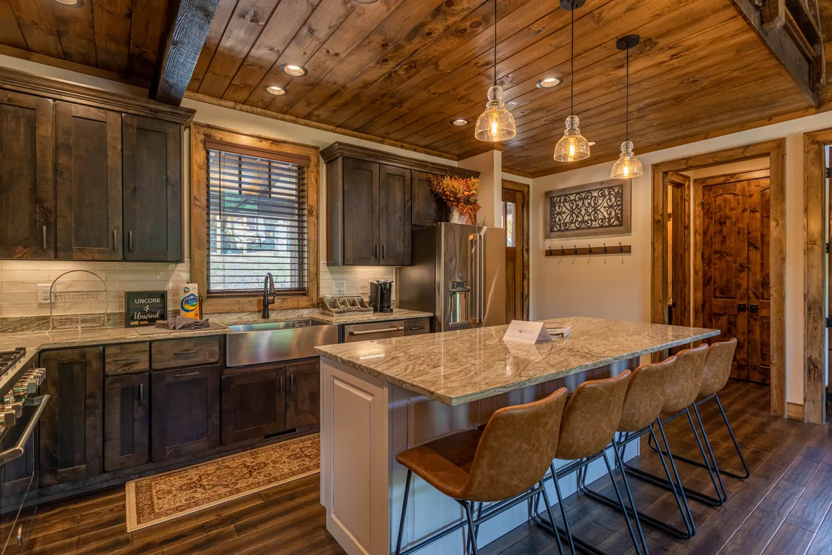 A cozy, rustic kitchen scene focusing on a granite countertop breakfast bar, wooden cabinetry, and pendant lighting. Bar stools invite casual dining or coffee moments, and the warm tones create a homely ambiance.