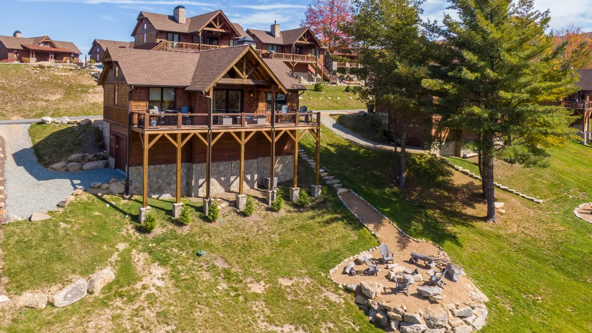 This image presents the exterior of a welcoming wooden house with an inviting outdoor seating area and a landscaped yard. The scene suggests opportunities for outdoor gatherings, relaxing around a fire pit, and enjoying the natural surroundings, all under a warm evening sky.