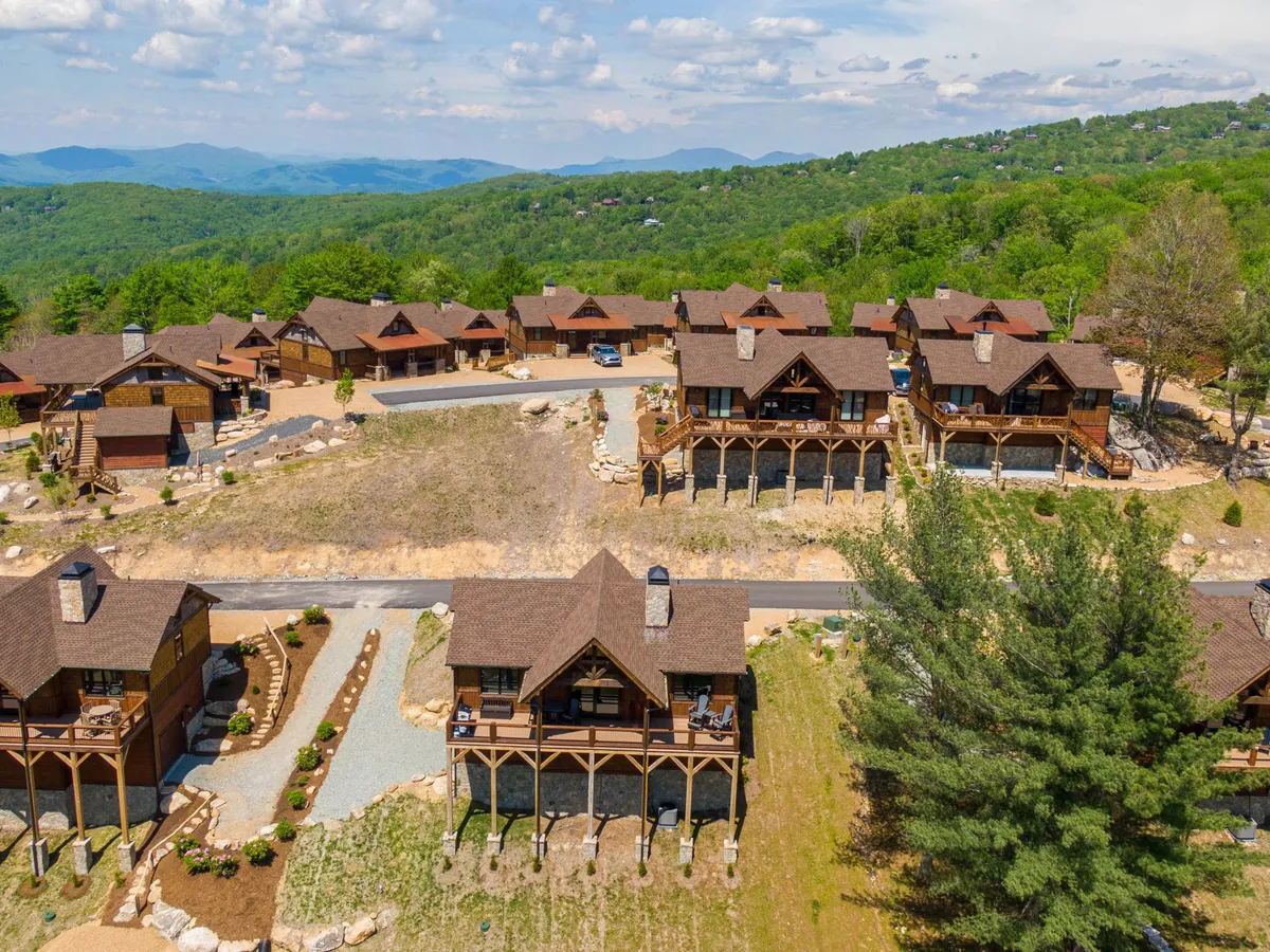 A view of several wooden cabins arranged along a landscaped garden with a majestic mountain backdrop and a paved road. The space is ideal for outdoor relaxation, family gatherings, and nature exploration, promoting a sense of community and connection to nature.