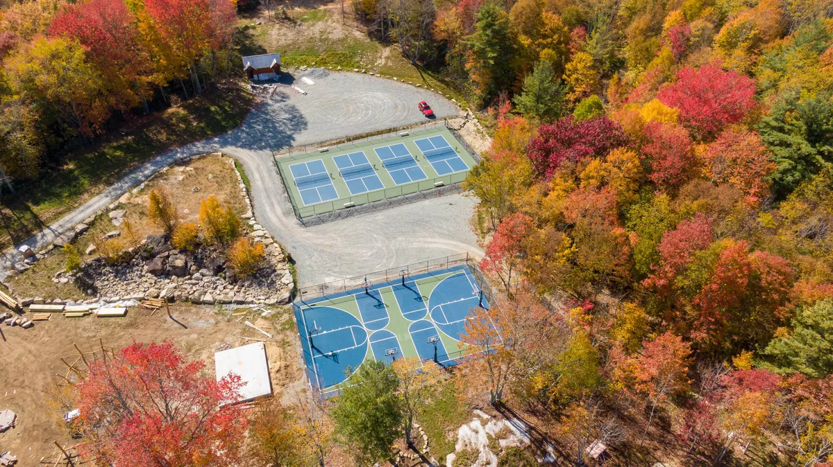Featuring basketball and tennis courts surrounded by autumn foliage, this energetic exterior image captures guests engaging in friendly competitions and gatherings amidst the beautiful landscape. The parking area hints at easy accessibility to amenities.